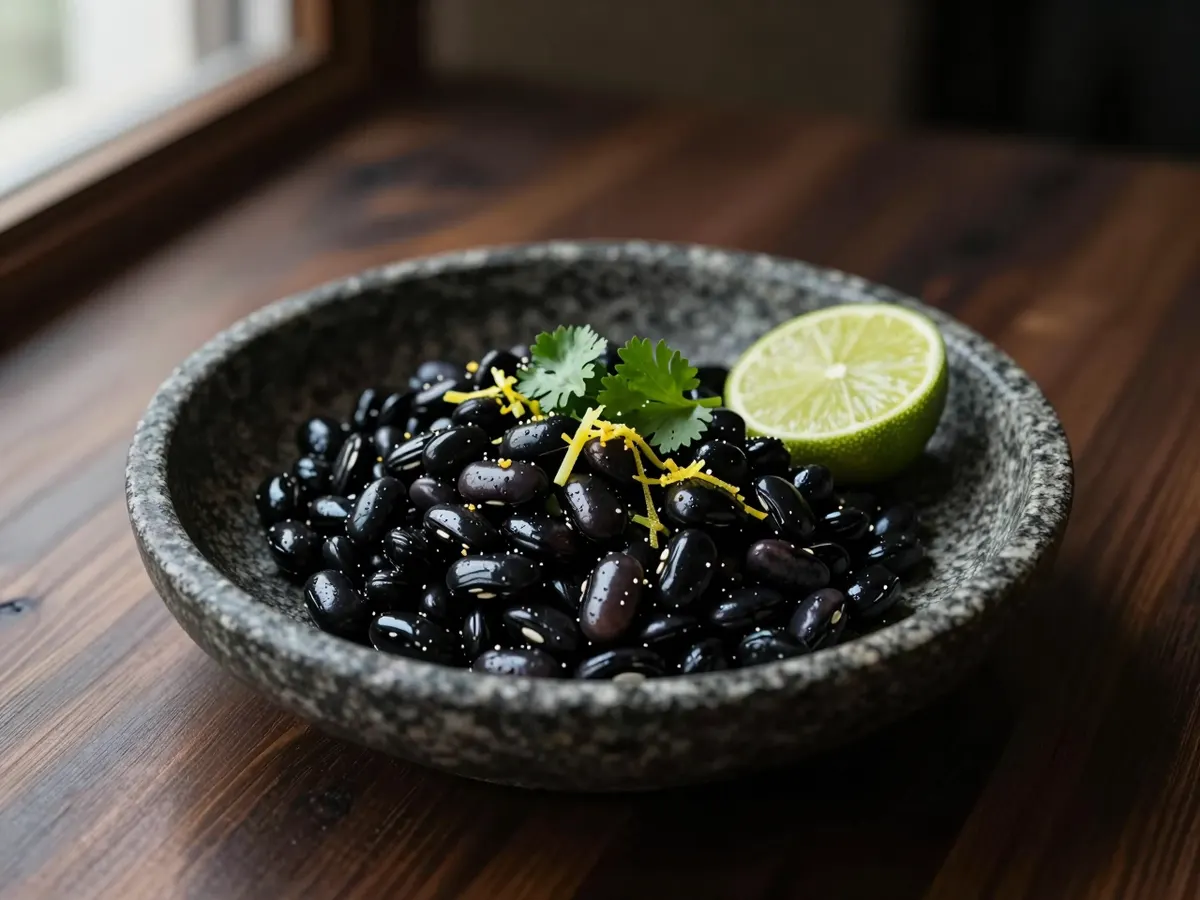 AI-generated photograph: Glossy black beans spooned into a small hand-thrown stone bowl, a scatter of bright green coriander, fine lime zest and a lime half on the side