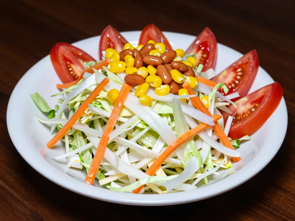 AI-generated photograph: A tall loose pile of fine white cabbage, lettuce and grated carrot on a wide shallow white bowl, bright stripes of yellow sweetcorn and orange baked beans across the top, red tomato wedges around the rim